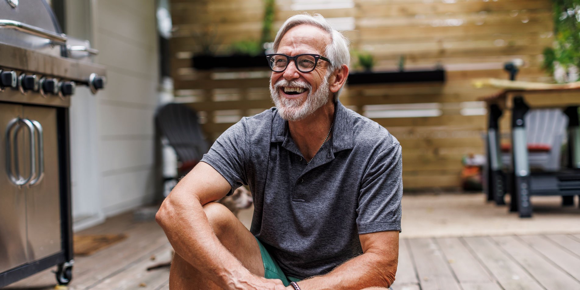 smiling man with white hair and beard sitting on wooden patio deck