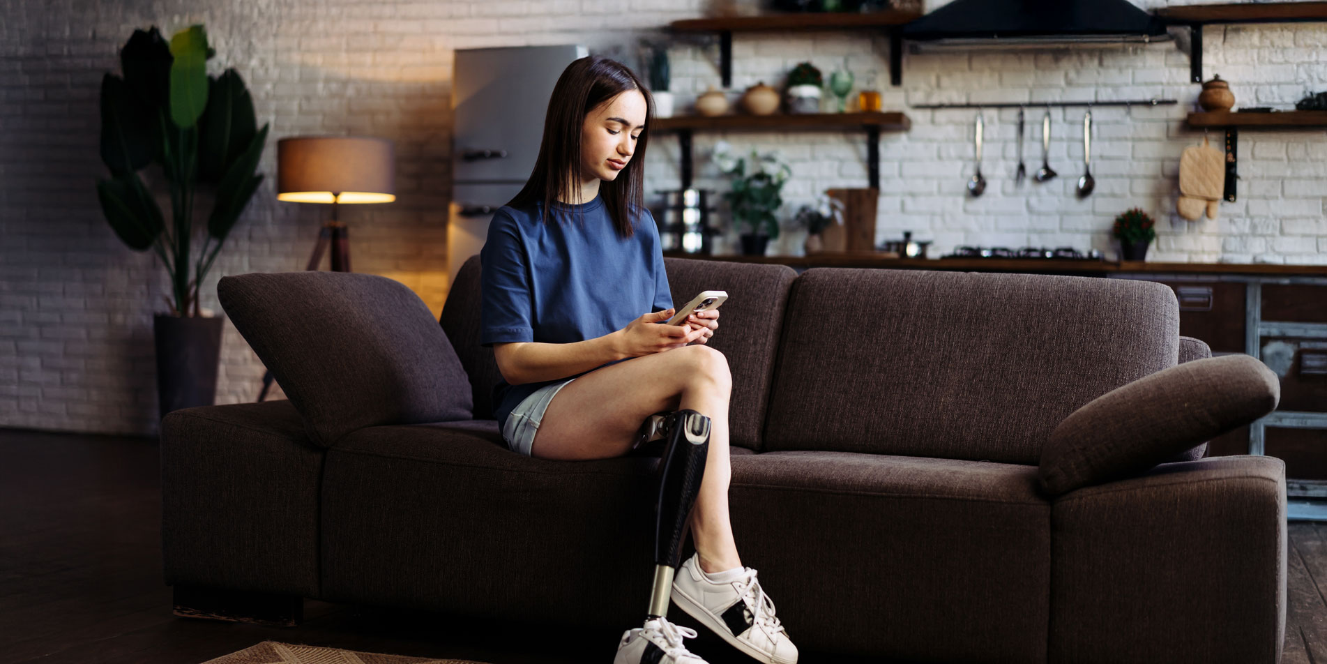 woman with prosthetic leg sitting on couch looking at phone