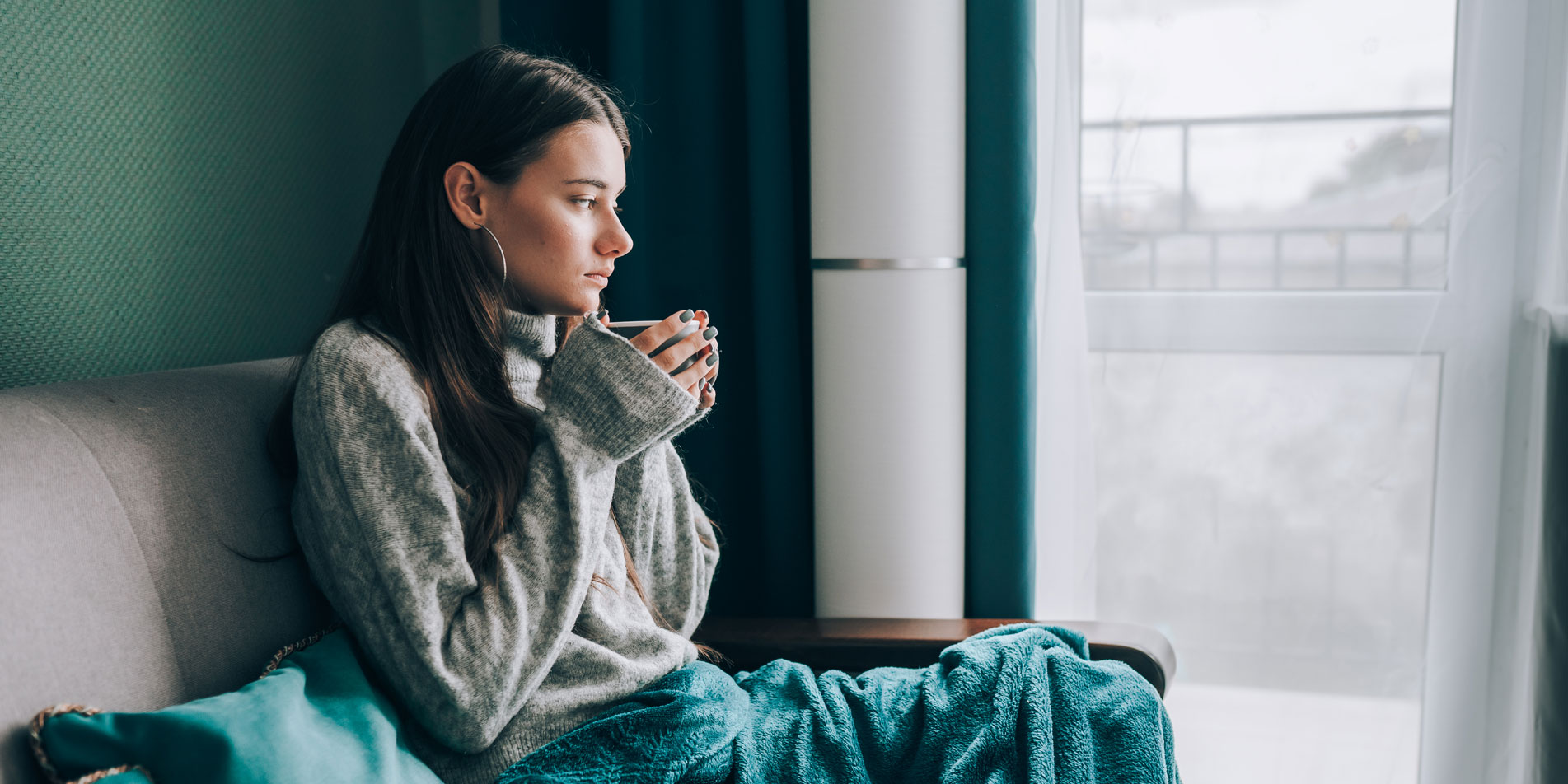 woman on couch holding mug looking out the window