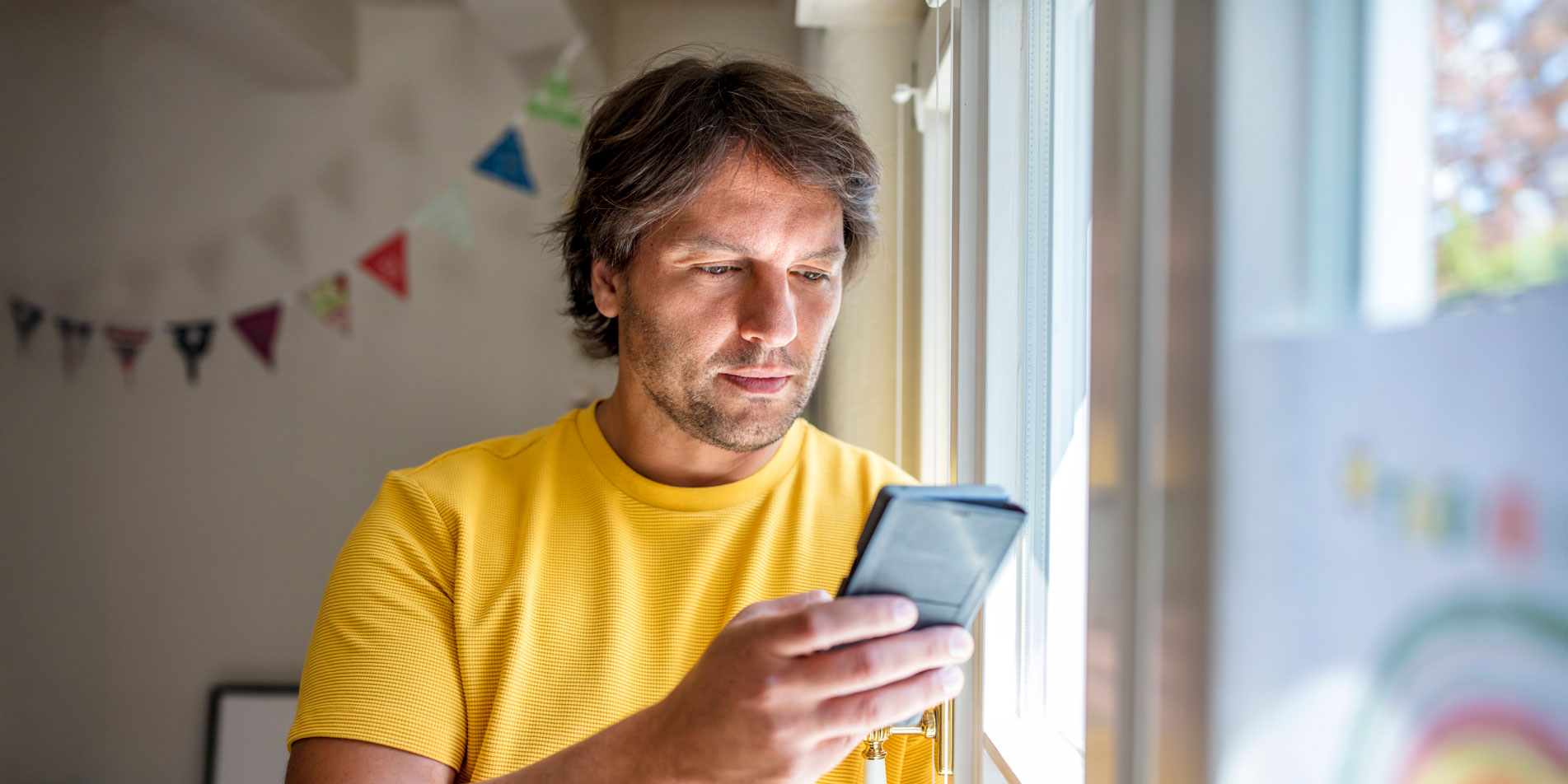 man standing at window using a mobile phone