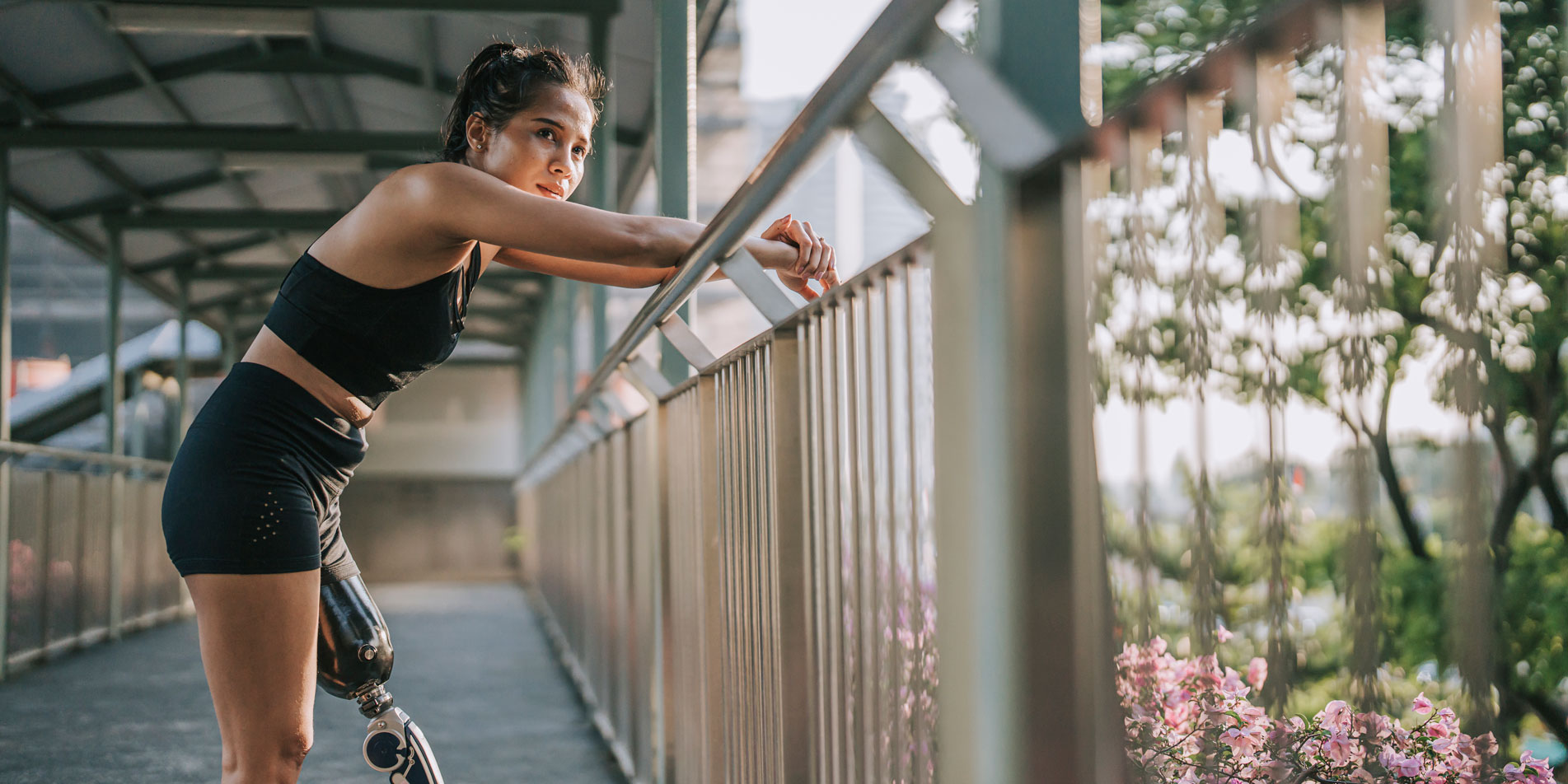 Asian female athlete with prosthetic leg resting leaning at footbridge