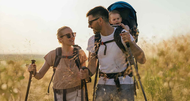 father carrying baby in backpack and mother hiking in a field