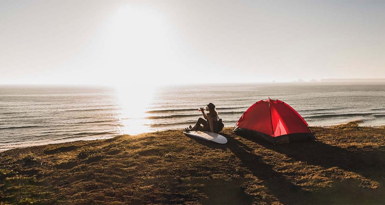 woman camping by the ocean at sunset