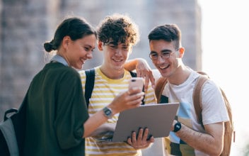 ausbildung-vertrieb-schnuppern_352x220_2023_12 Glückliche Studenten, die gemeinsam ein Mobiltelefon und einen Laptop-Computer benutzen, während sie im Freien stehen