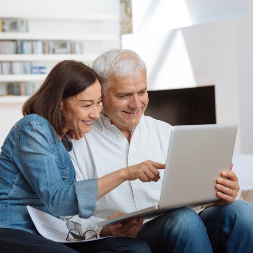 Paar sitzt zusammen auf einem Sofa und schaut gemeinsam auf Laptop