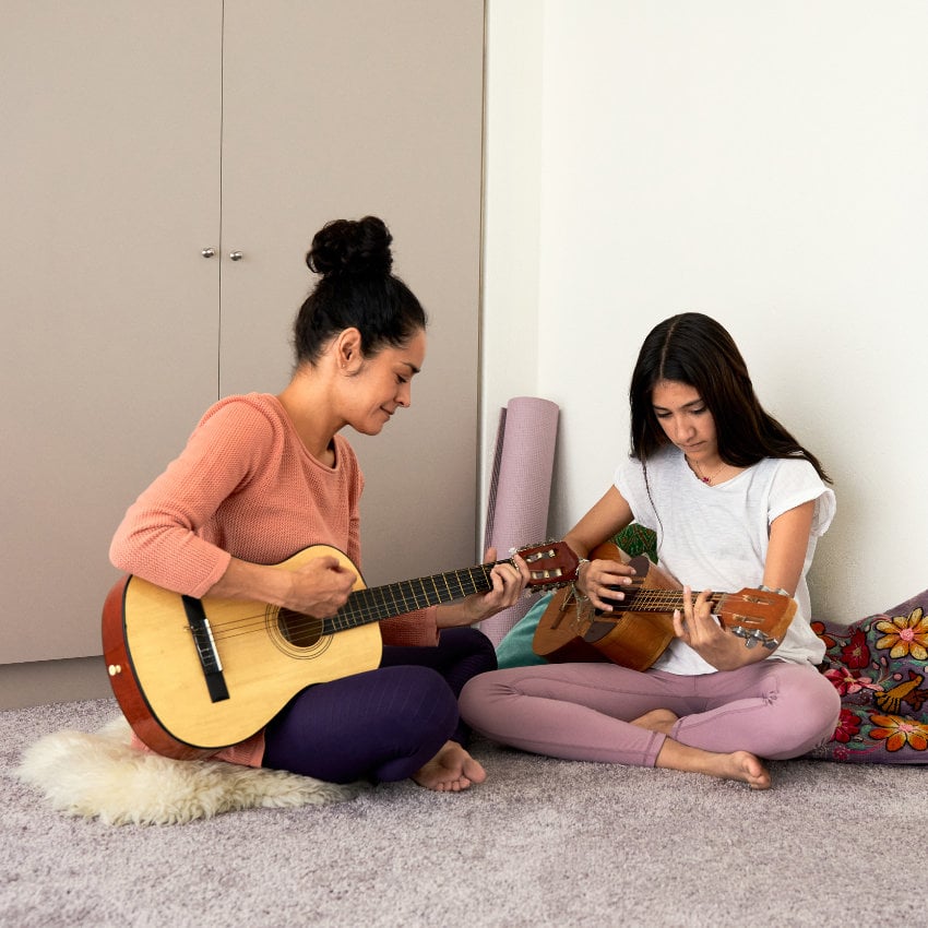 Colombia_mother_daughter_music_carmentrianaa Zwei Frauen sitzen im Schneidersitz auf dem Boden und spielen Gitarre