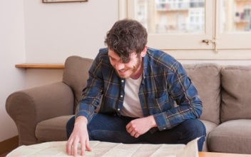 junger Mann sitzt über Landkarte gebeugt auf Sofa