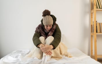 Frau sitzt frierend mit Mütze und Winterjacke in ihrer Wohnung