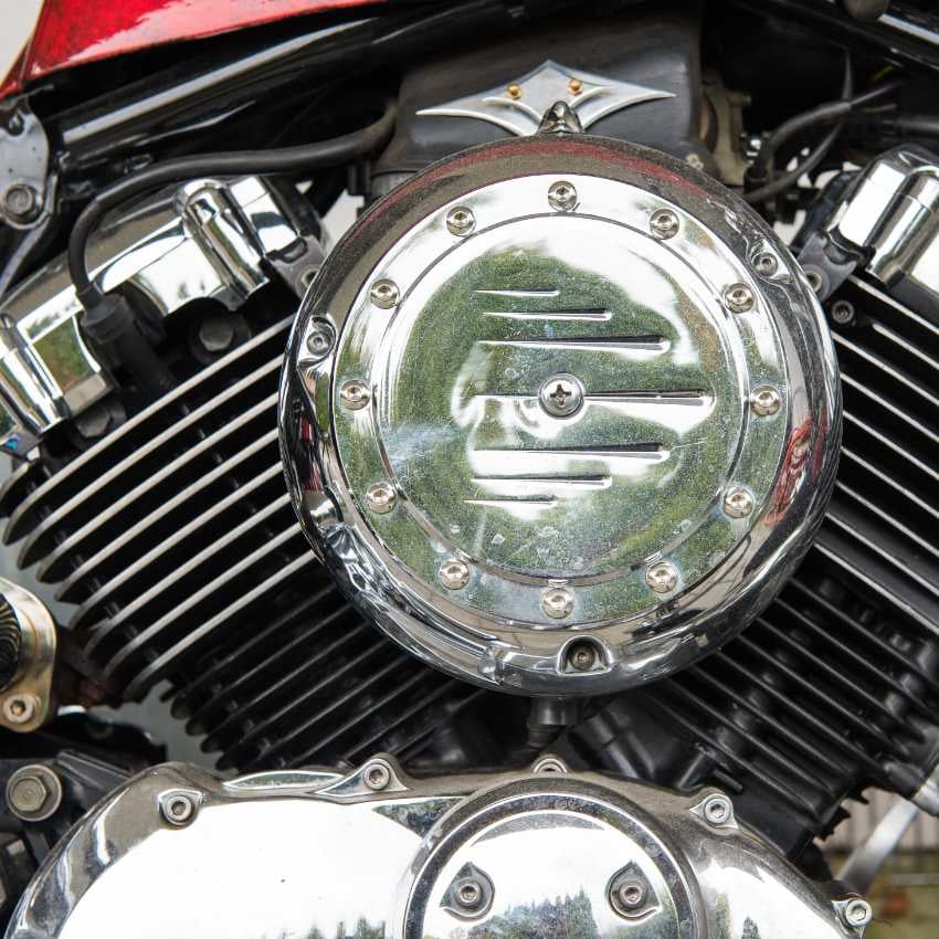Frau mit Sonnenbrille sitzt vor einem roten Motorrad auf einer Straße im herbstlichen Wald