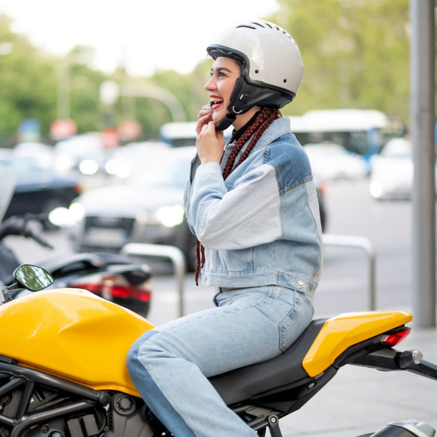 GettyImages-1316464278 Frau auf gelbem Motorrad setzt sich ihren Motorradhelm auf