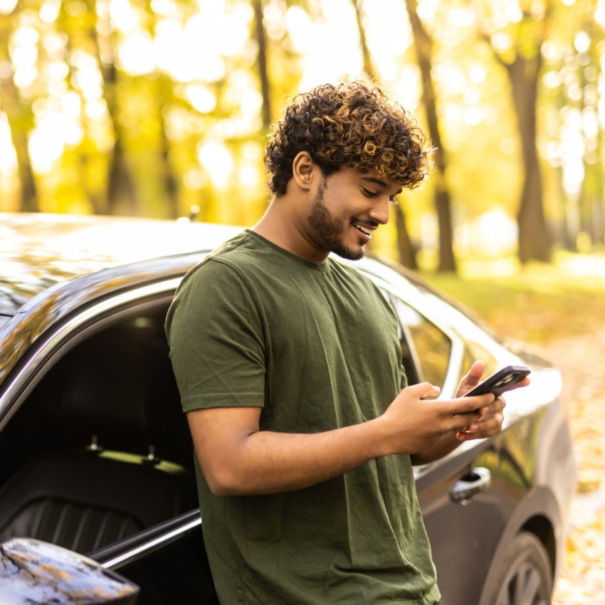 Mann lehnt an seinem Auto und schaut aufs Handy