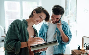 Telefonierender Mann mit Frau, die am Pad arbeitet