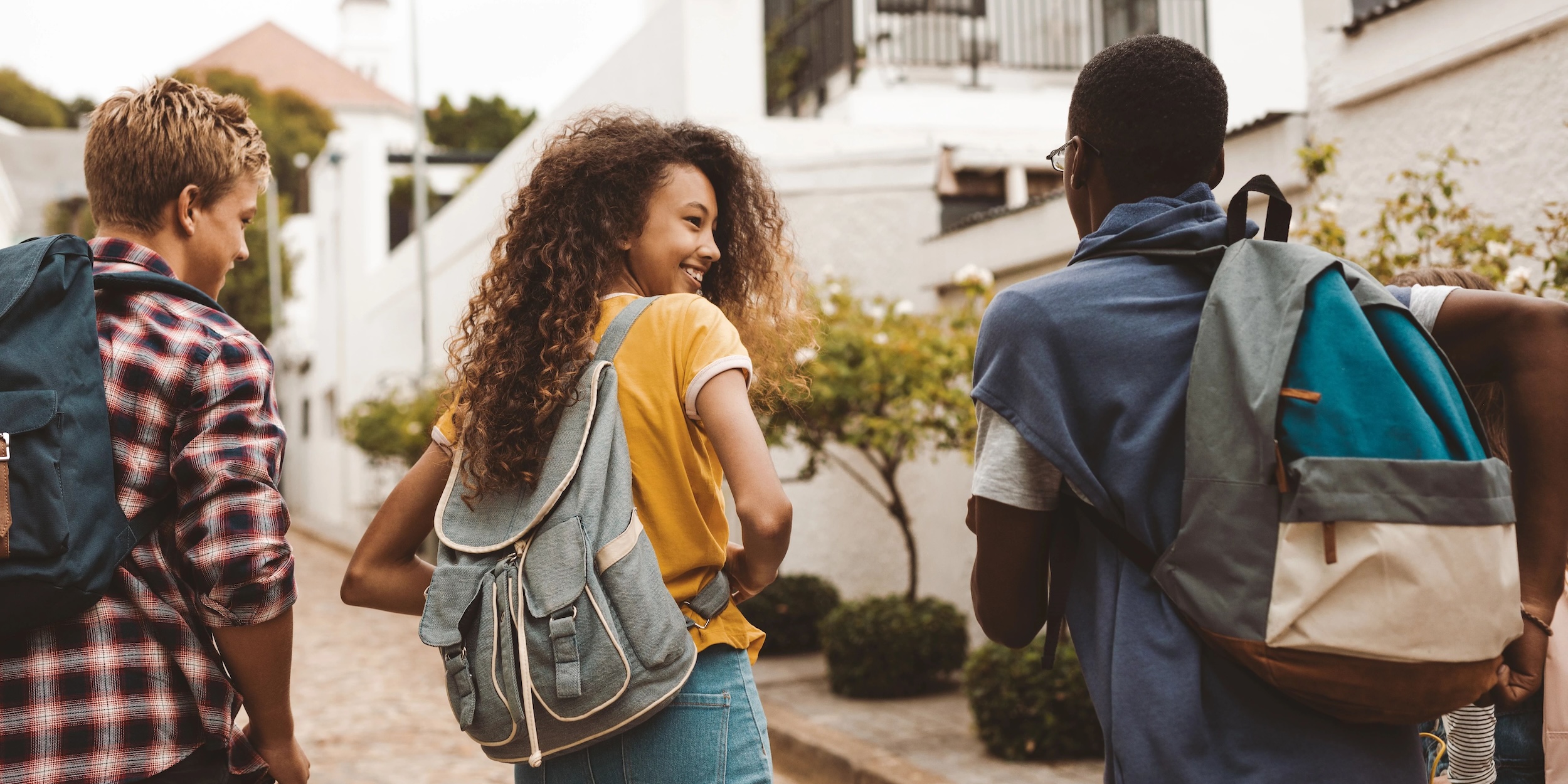 A girl and three boys wearing backpacks and walking
