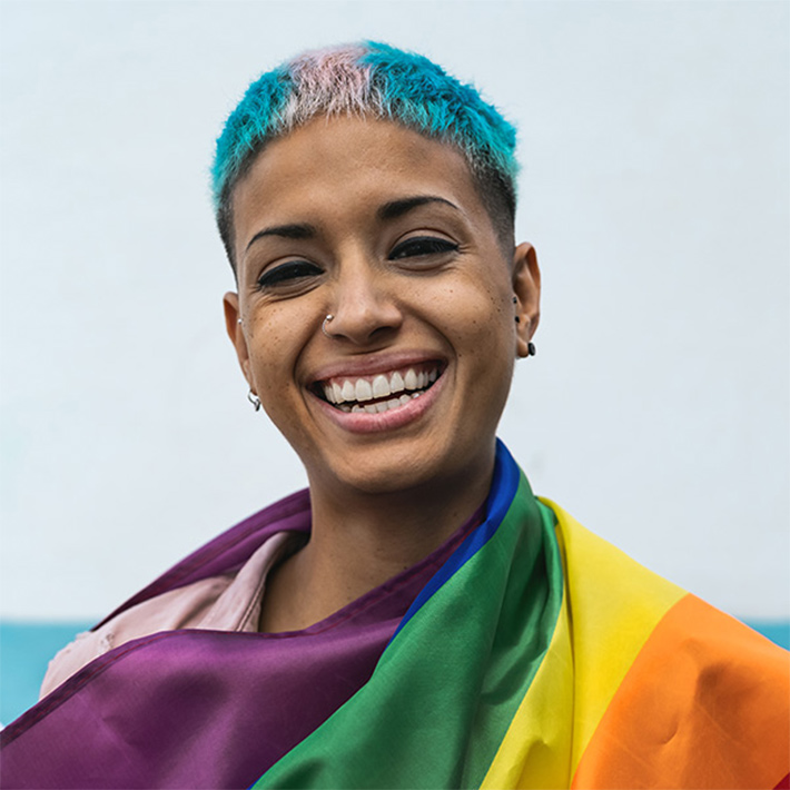 a smiling woman with the lgbtq+ flag over her shoulders