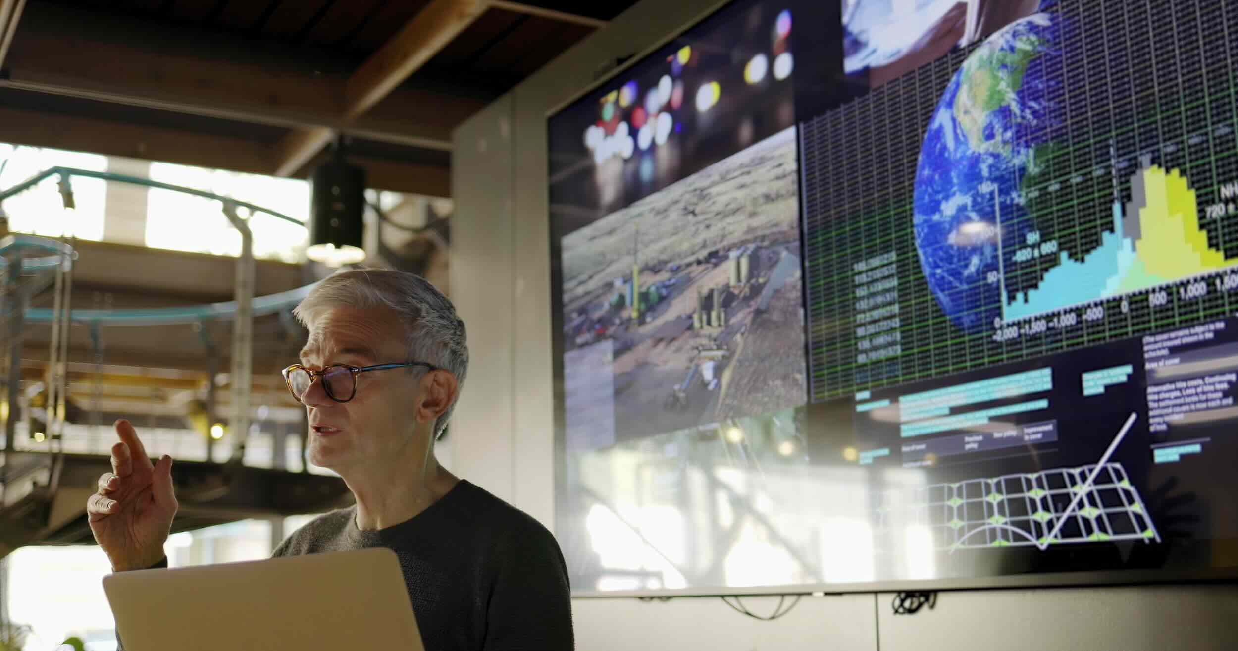 Man using a laptop with large screen behind him