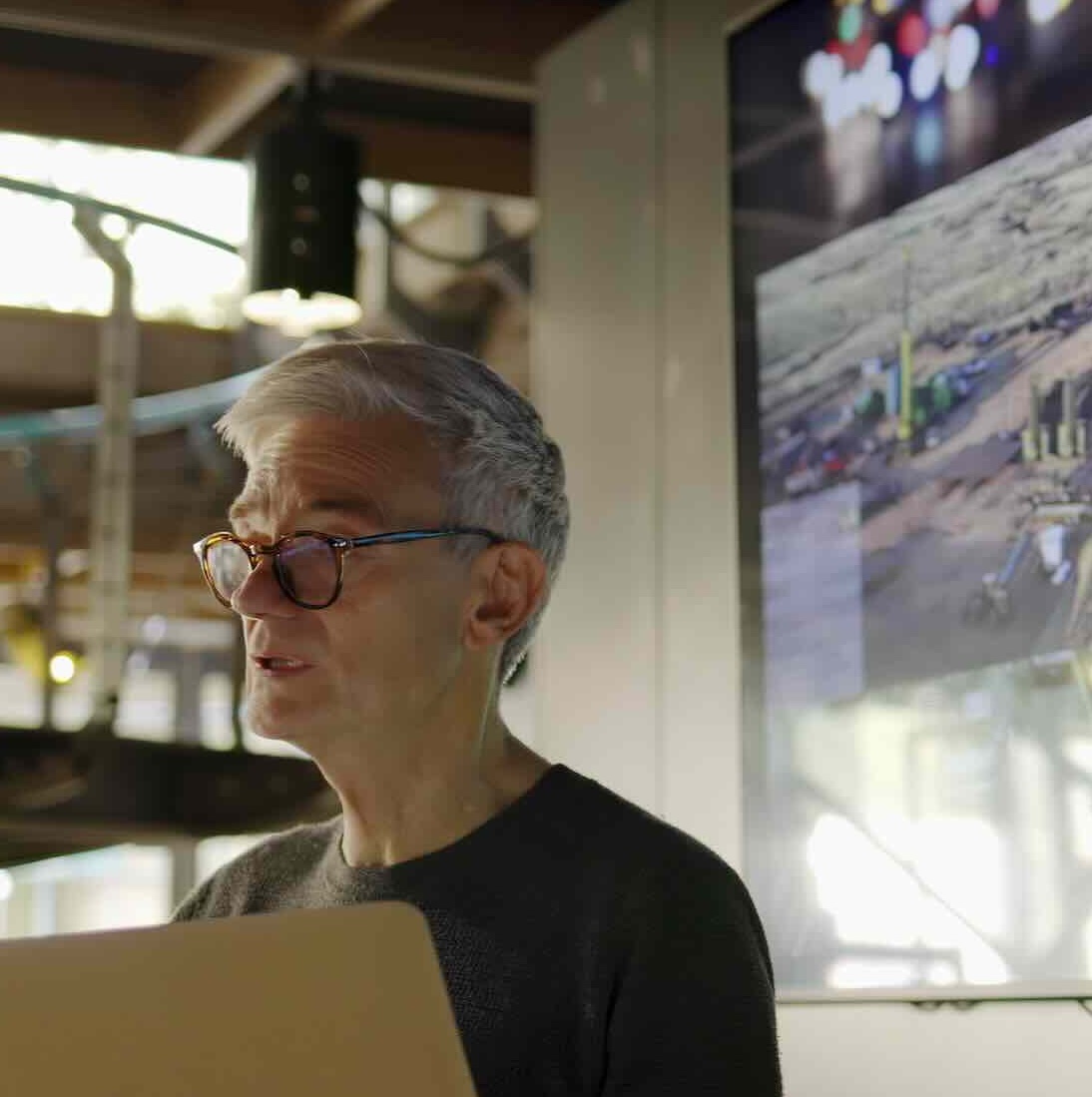 Man using a laptop with large screen behind him