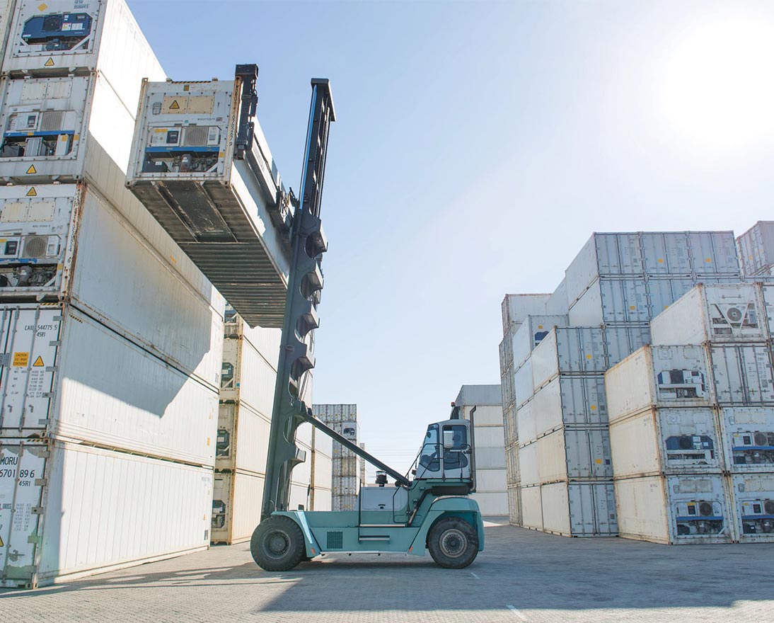 Forklift bringing down container in storage yard