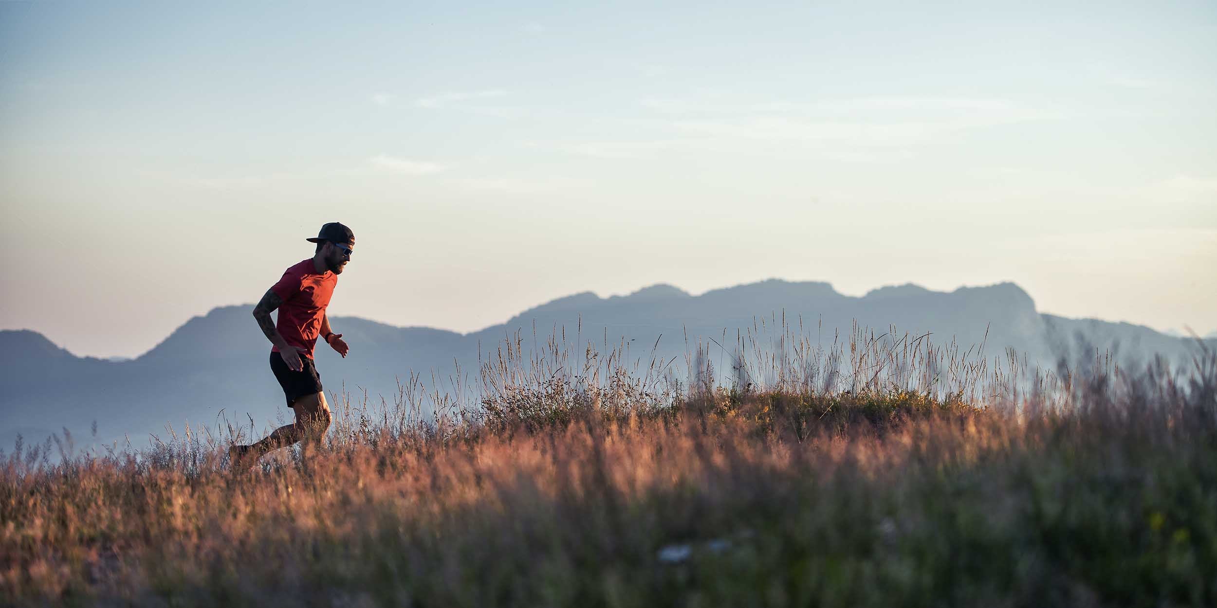 In a hilly sunset in colorful meadows a young sporty man runs alone