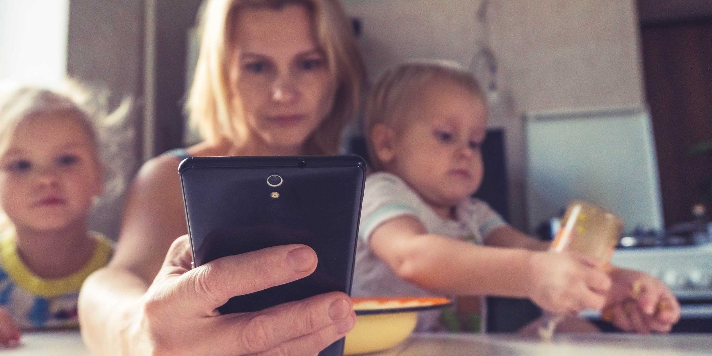woman looking at her phone with two children by her side