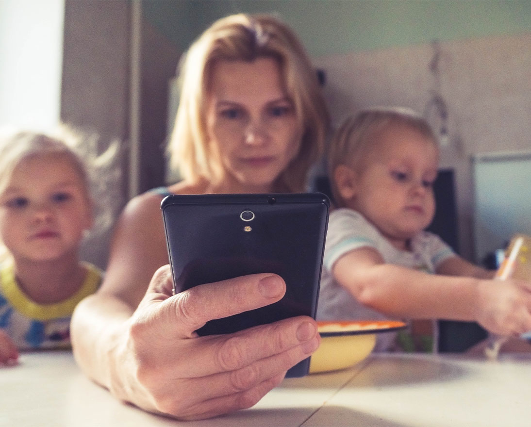 woman looking at her phone with two children by her side