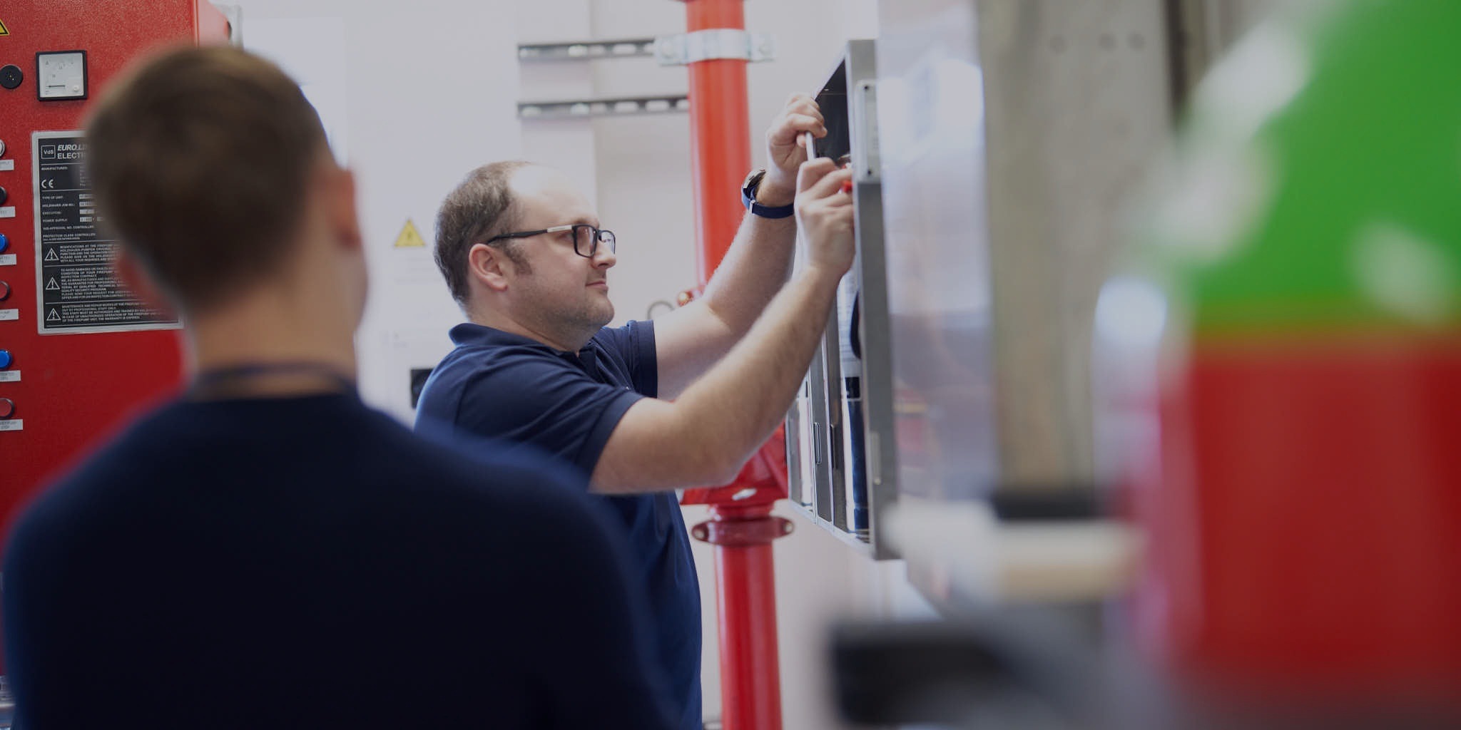 Two people working on industrial electrical panel.
