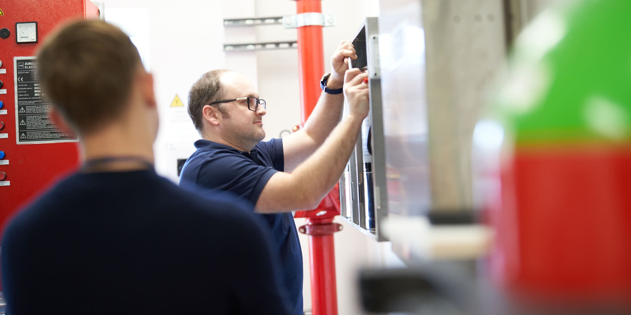 Two people working on industrial electrical panel.