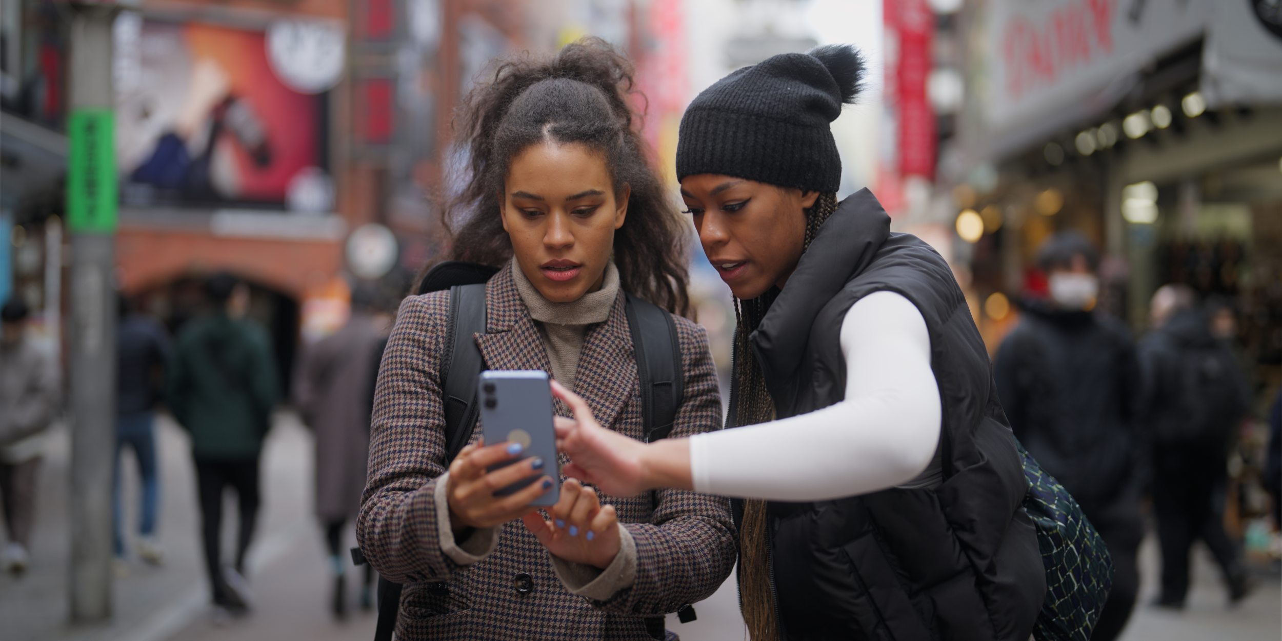 Two women using smartphone on busy street