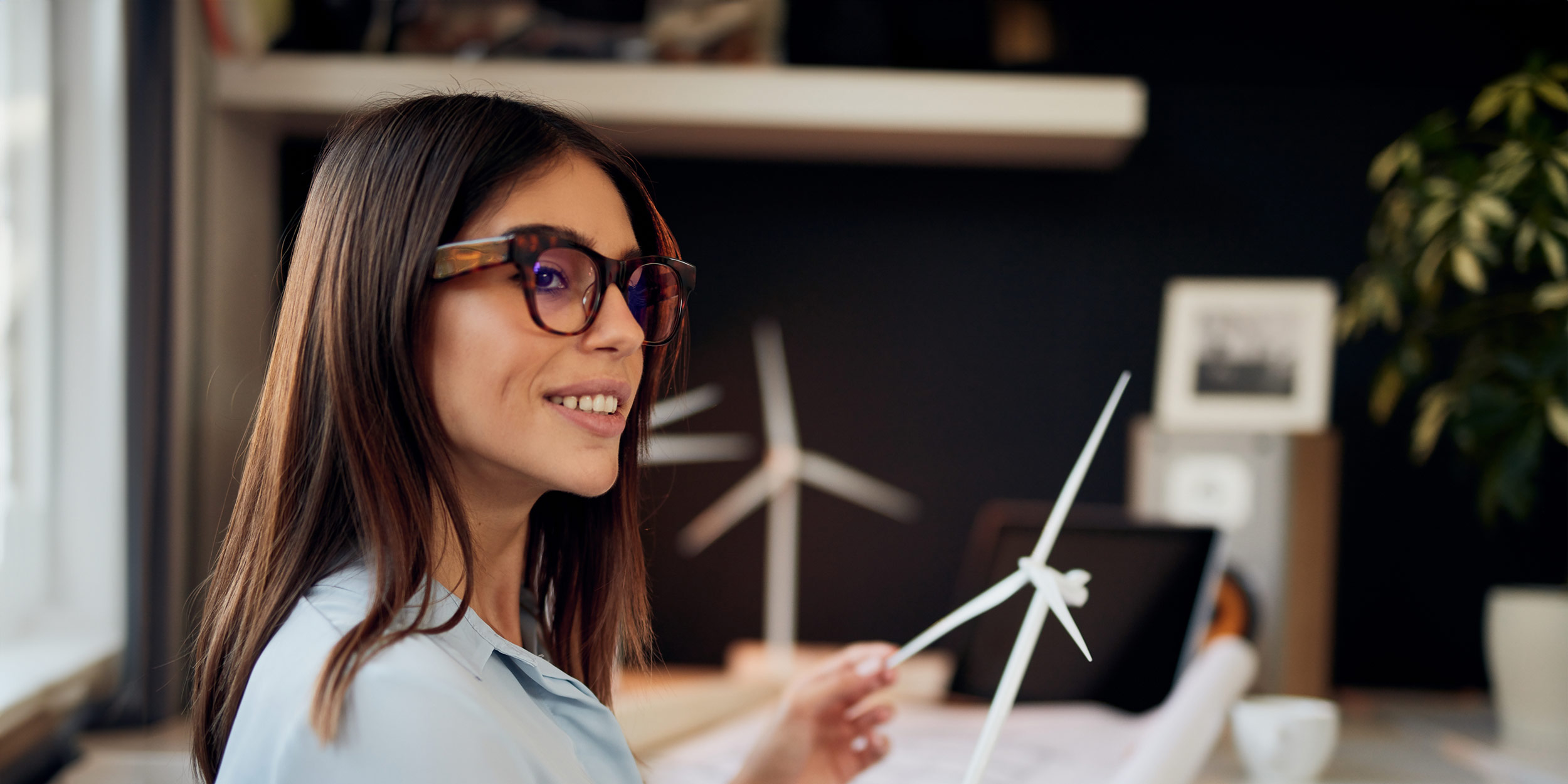 Businesswoman sitting in modern office and holding windmill model