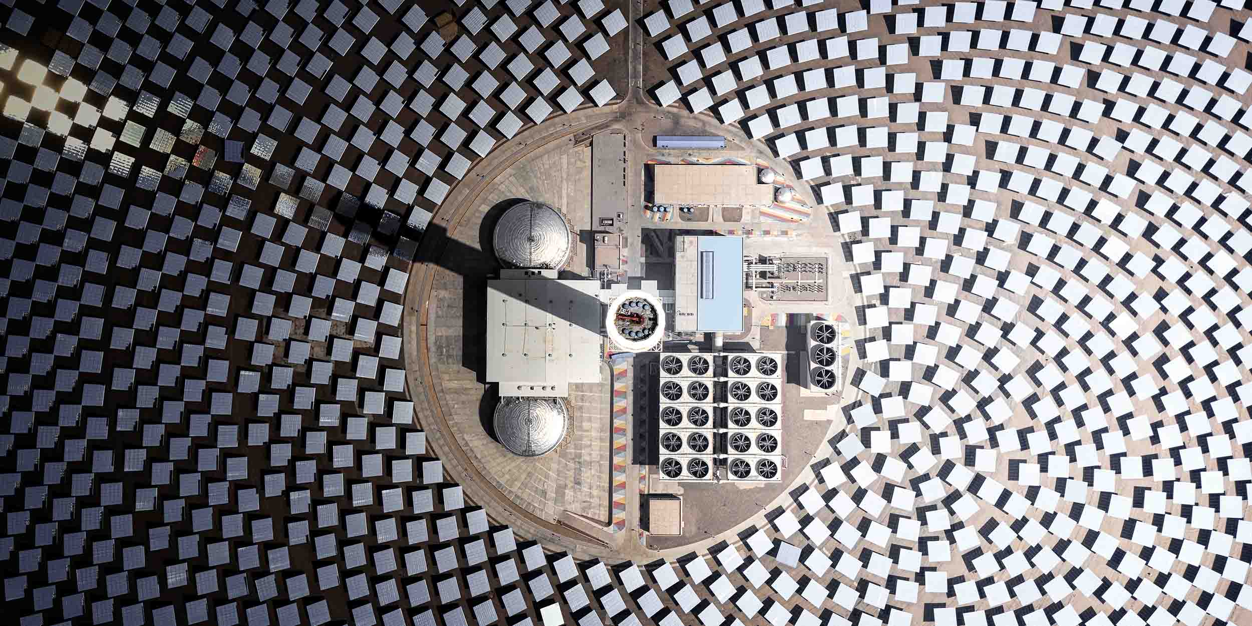 Aerial view of a solar power plant, with mirrors arranged in circular patterns around a central energy tower