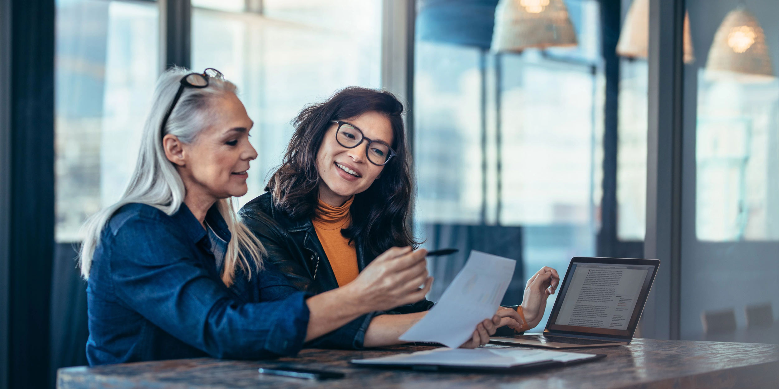 Two women analyzing documents while sitting on a table in office