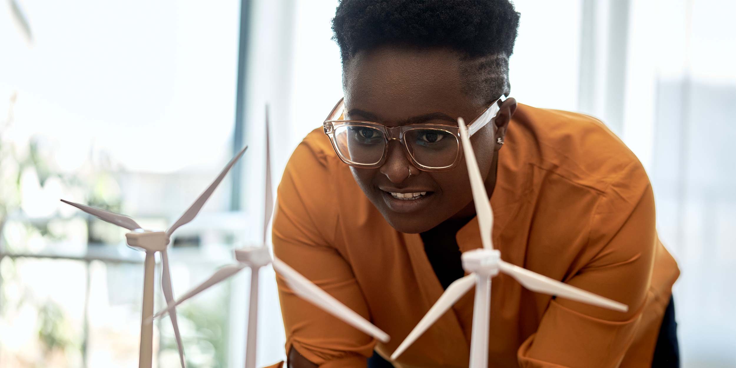 Woman wearing eyeglasses examining wind turbine models at office