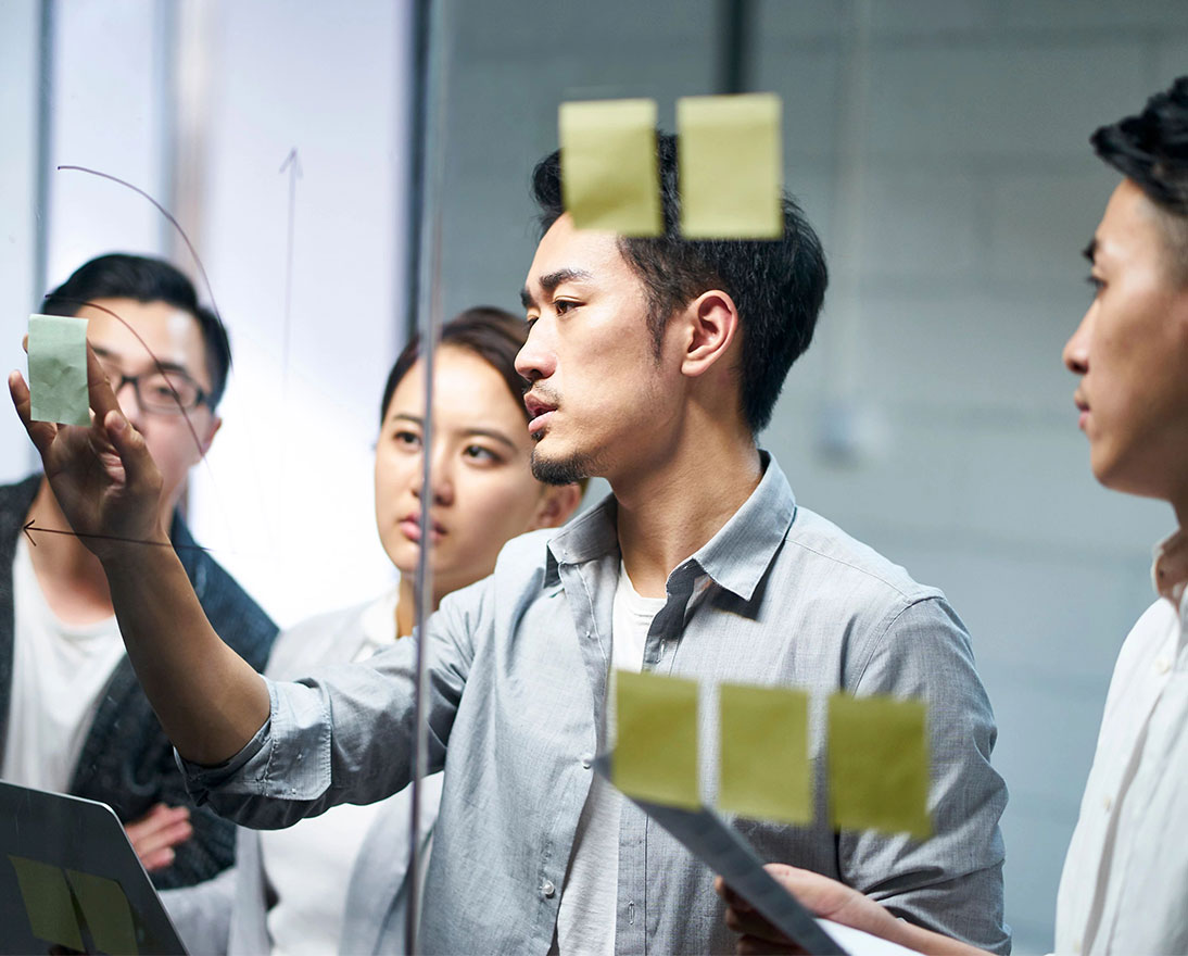 entrepreneur putting a note on glass during team meeting
