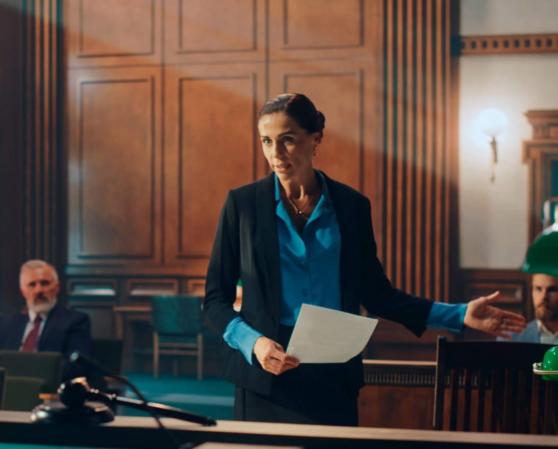 Lawyer presenting documents in a courtroom with judge and audience during trial proceedings.