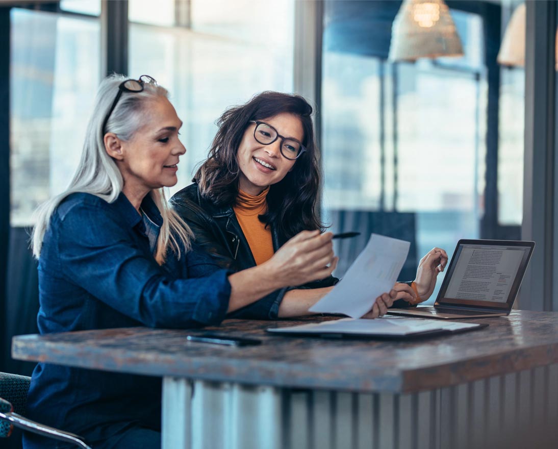 Two women analyzing documents while sitting on a table in office
