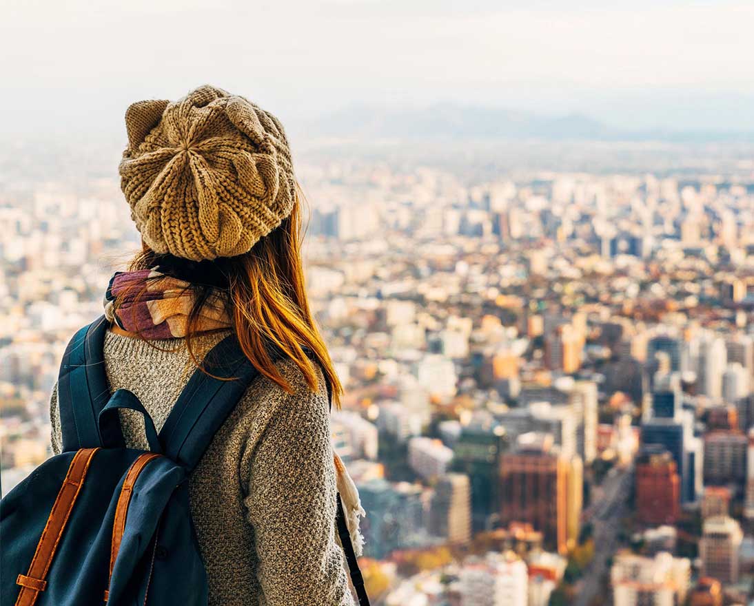 Woman with hat and backpack looking out over cityscape