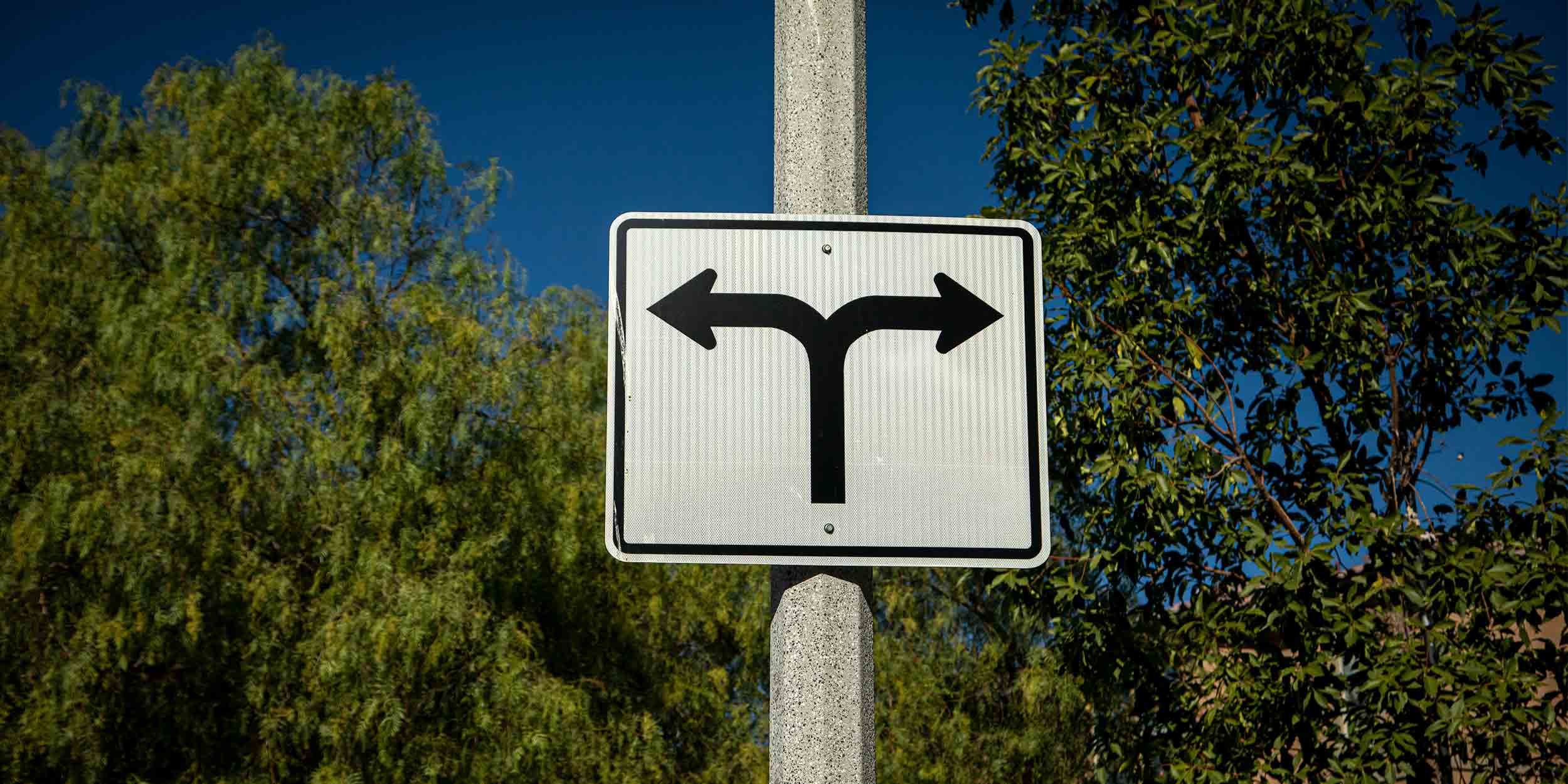 Road sign on a street pole with arrows pointed in opposite directions