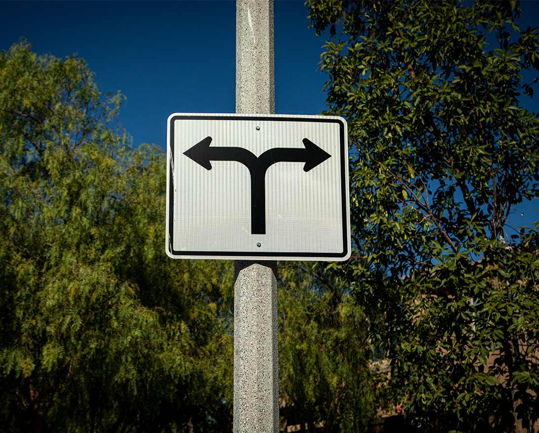 Road sign on a street pole with arrows pointed in opposite directions