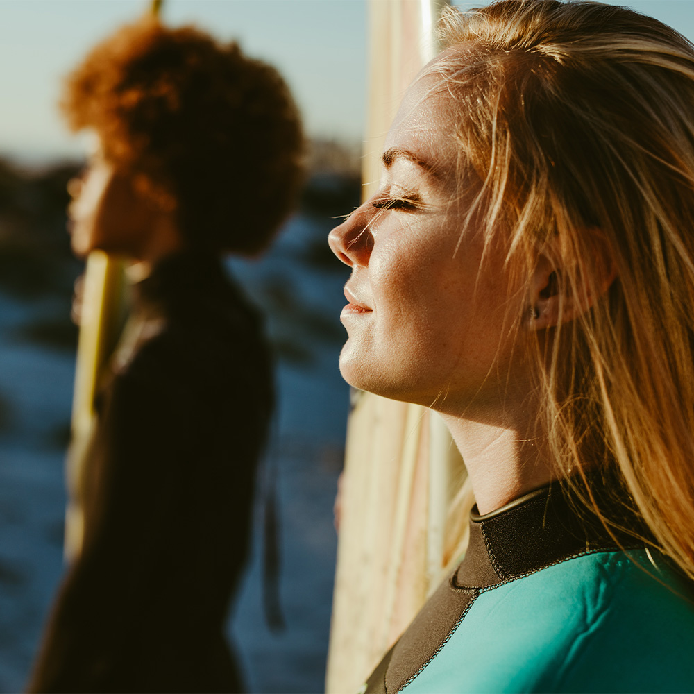 Two women on the beach with their surfboard soaking up the sunshine