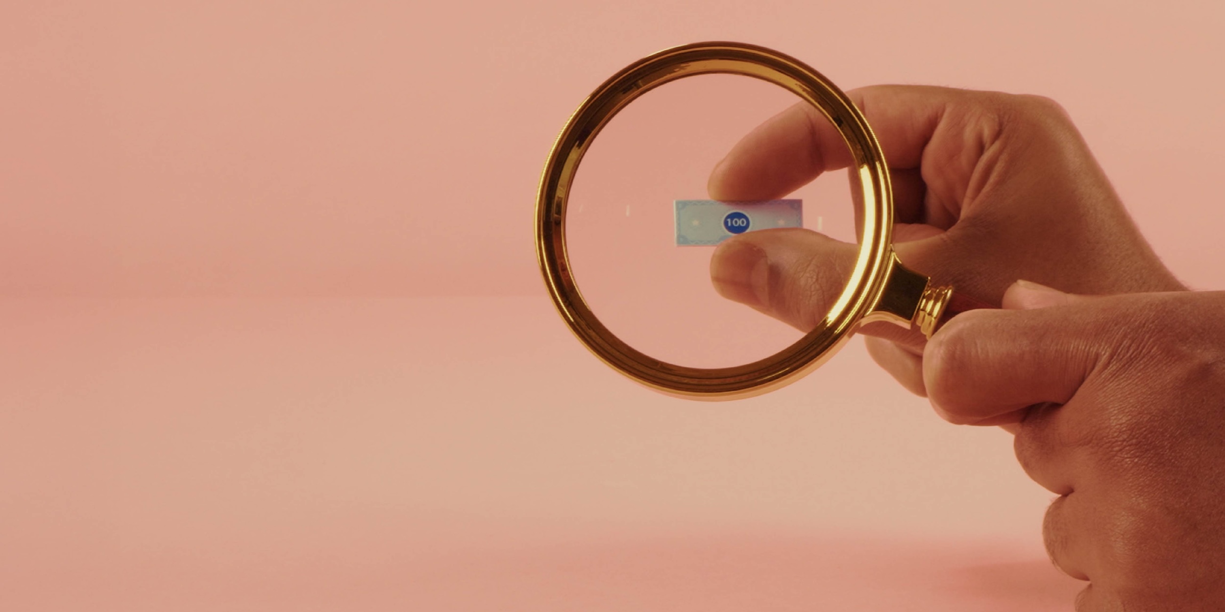 Hand holding a magnifying glass looking at 100 dollar bill
