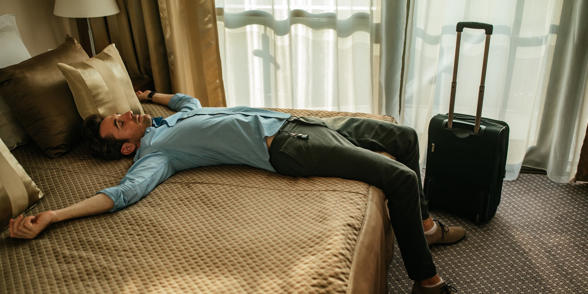 Man lying on hotel bed with jet lag