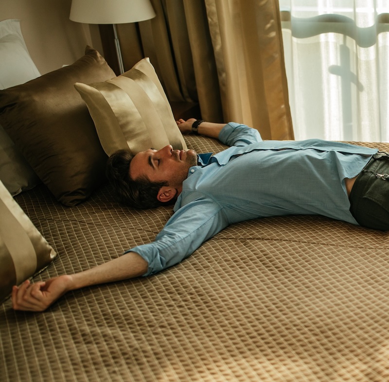 Man lying on hotel bed with jet lag