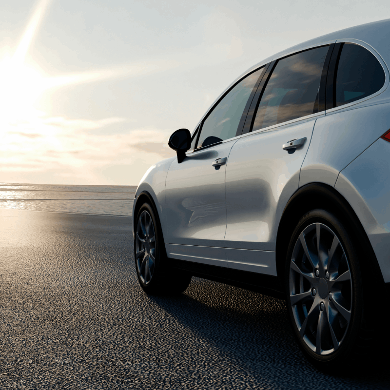 Sunlit car driving by the ocean.