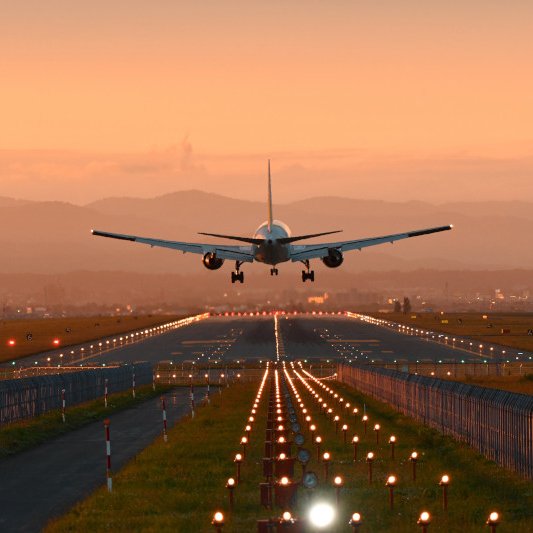 An airplane landing on a runway at sunset, with mountains in the background.