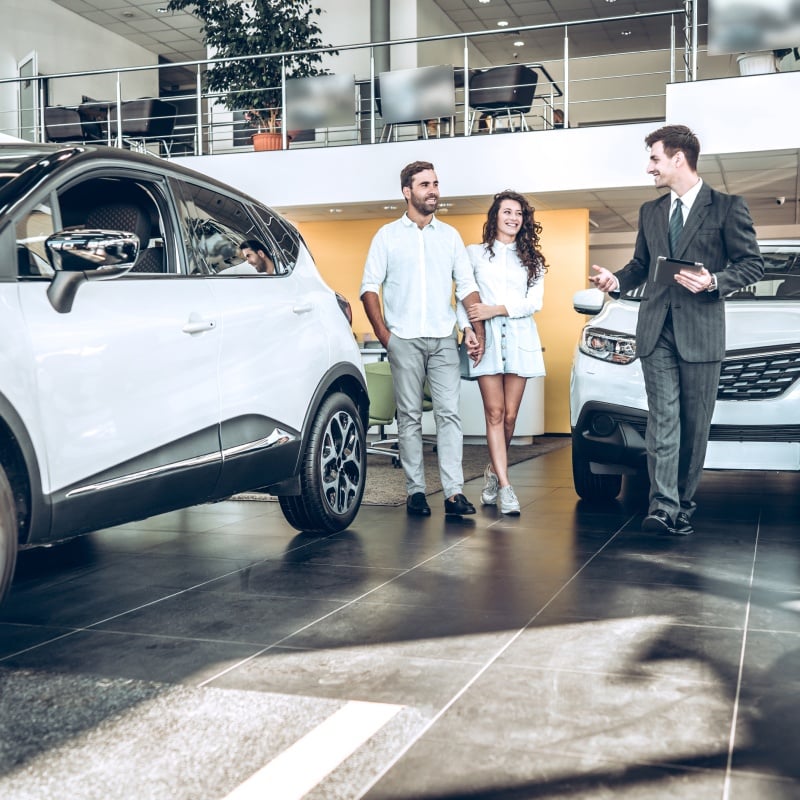 Couple talking with car dealer in showroom