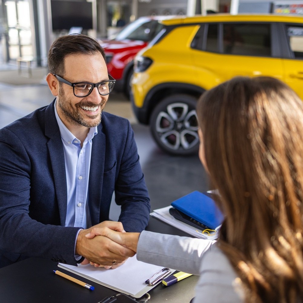 car dealership handshake over paperwork with cars