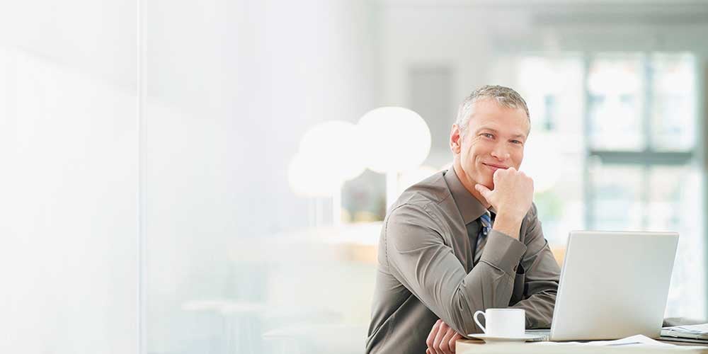 1000x500_guy-smiling-at-table-with-laptop guy smiling at table with laptop