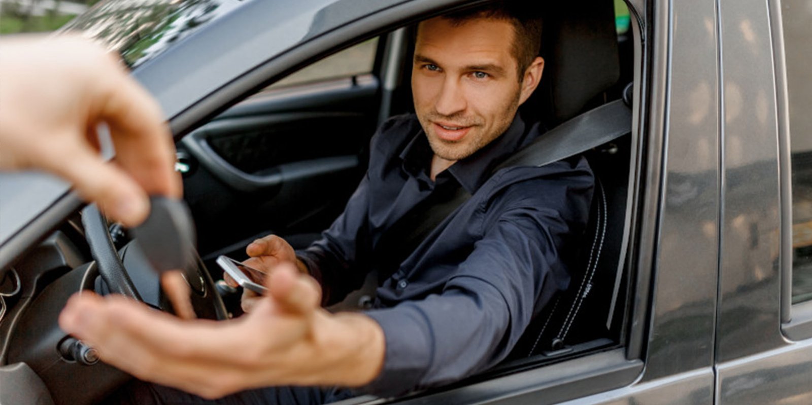 Mann sitzt im Auto und bekommt Autoschlüssel gereicht