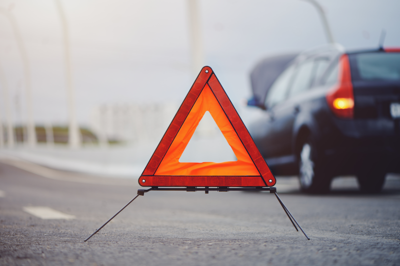 Nach einem Totalschaden steht das Auto mit Pannendreieck abgesichert am Fahrbahnrand