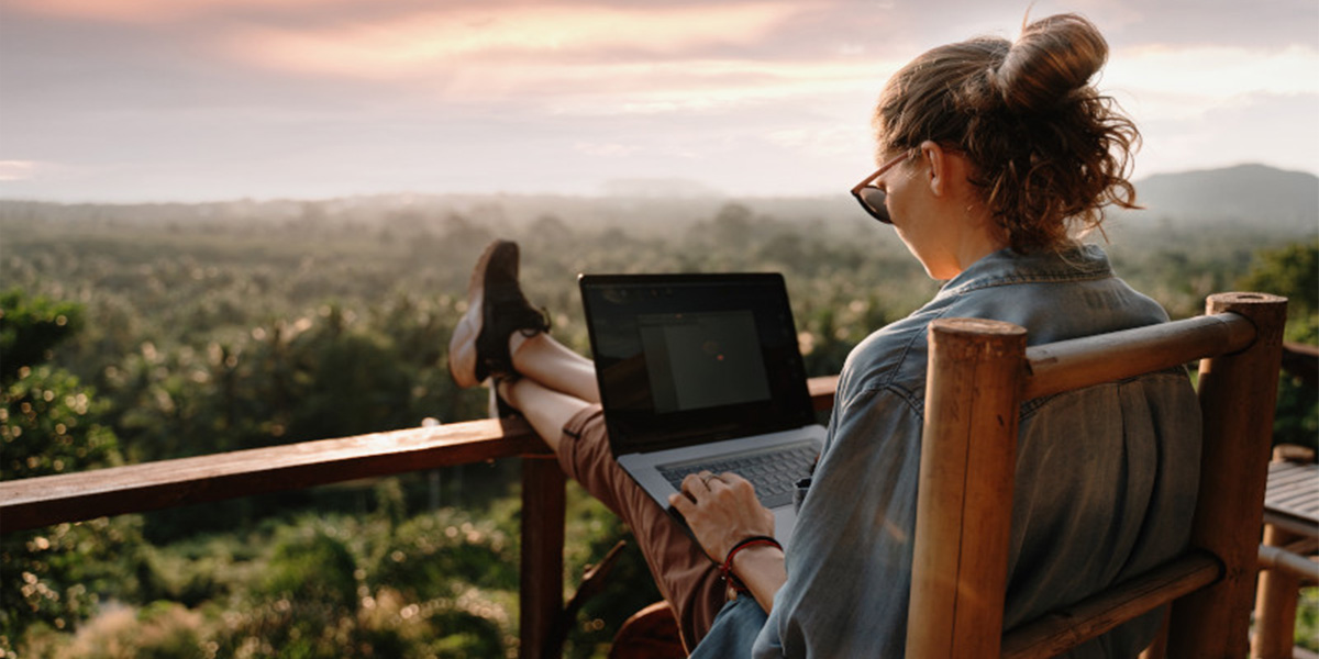 Dame sitzt in der Natur mit Laptop am Knie