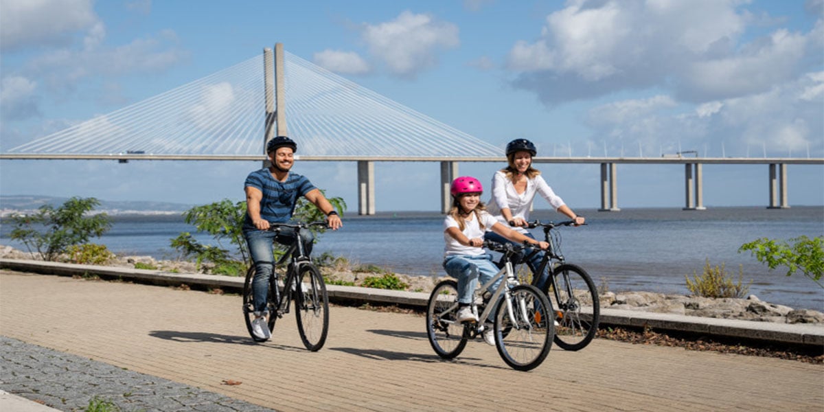 Eine Familie fährt mit drei Fahrrädern entlang eines großen Flusses | Zurich Connect Fahrradversicherung